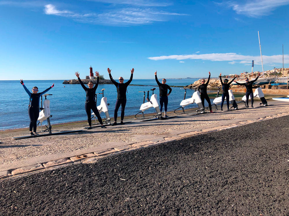 A group of riders raising their arms beside their Hydrofoiler bikes on a stony shoreline